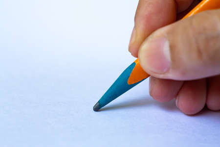 Woman's right Hand holding multicoloured pencil, writing letter on white paper texture background, Notebook, Close up & Macro shot, Selective focus, Communication, Stationery conceptの写真素材