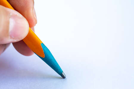 Woman's left Hand holding multicoloured pencil, writing letter on white paper texture background, Notebook, Close up & Macro shot, Selective focus, Communication, Stationery conceptの写真素材