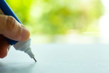 Woman's holding blue Liquid Correction Writing Pen or liquid for correct hand writing mistakes on white paper in bokeh green garden  Background, Close up & Macro shot, Selective focus, Office Stationery conceptの写真素材