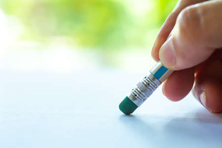 Woman's right Hand hold multicoloured pencil, Green rubber to delete from white paper, Bokeh green garden background, Notebook, Close up & Macro shot, Select focus, Communication, Stationery conceptの写真素材
