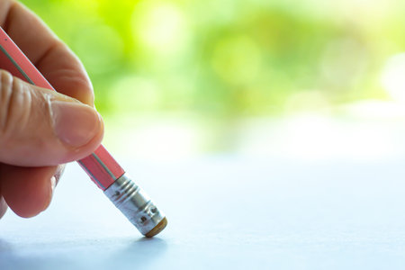 Woman's left Hand hold multicoloured pencil, White rubber to delete from white paper, Bokeh green...