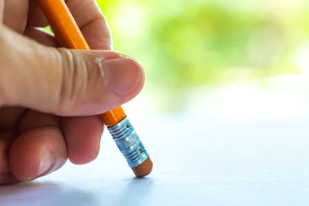 Woman's left Hand hold orange riangular pencil, Rubber to delete from white paper, Bokeh green garden background, Notebook, Close up & Macro shot, Selective focus, Communication, Stationery conceptの写真素材