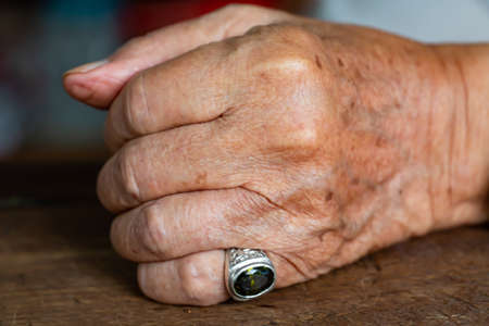 Senior man's left hand in fist on wood table background, Mole and blemish, Close up & Macro shot, Selective focus, Asian body skin part, Symbol, Gesturing, Body Language Conceptの写真素材
