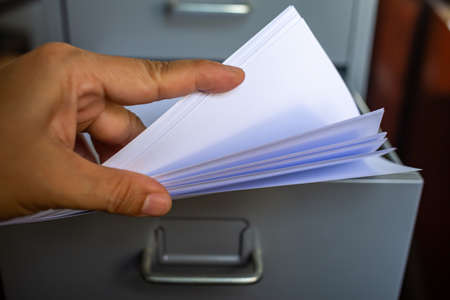 Woman's hand pick up white papers for write letter, Filing cabinet with open drawer, Grey silver metal colour, Administration and storage concept, closeup & Macro shot, Selective focusの写真素材
