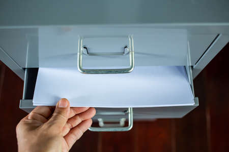 Woman's hand pick up white papers for write letter, Filing cabinet with open drawer, Grey silver metal colour, Administration and storage concept, closeup & Macro shot, Selective focusの写真素材