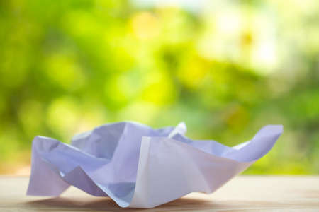 Crumpled white paper on wood table, Bokeh green garden background, Close up & Macro shot, Selective focus, Brainstorming, Creative idea, Business conceptの写真素材