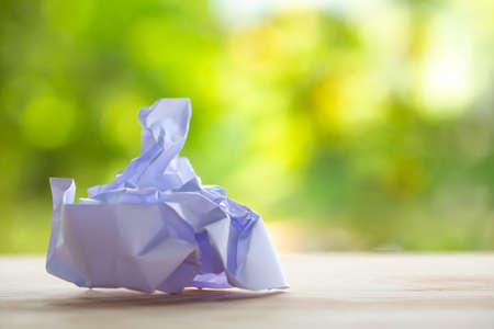 Crumpled white paper on wood table, Bokeh green garden background, Close up & Macro shot, Selective focus, Brainstorming, Creative idea, Business conceptの写真素材