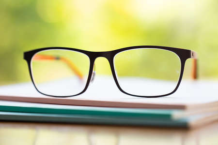 Black eyeglasses with three white notebook on wooden table, Bokeh garden background, Close up & Macro shot, Selective focus, Stationery conceptの写真素材