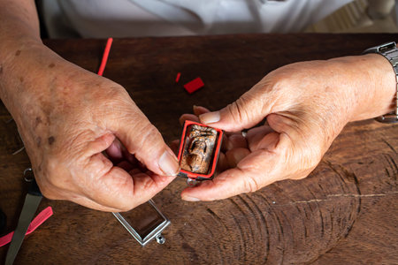 Senior man' s hands to provide Amulet, Small Buddha image with a metal cap on wood table texture...