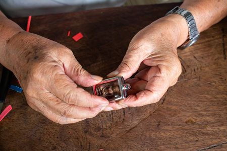Senior man' s hands to provide Amulet, Small Buddha image with a metal cap on wood table texture...