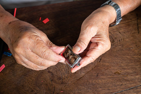 Senior man' s hands to provide Amulet, Small Buddha image with a metal cap on wood table texture...