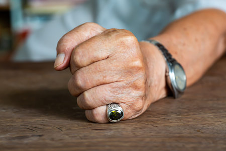 Senior man's left hand in fist on wood table background, Mole and blemish, Close up & Macro shot,...