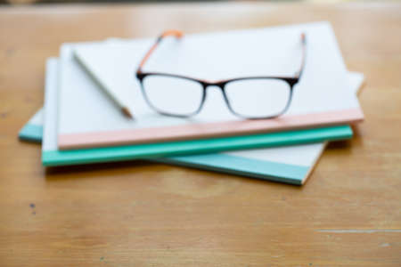 Blurred black eyeglasses, white pencil with three white notebooks on wooden table, Close up & Macro shot, Stationery conceptの写真素材