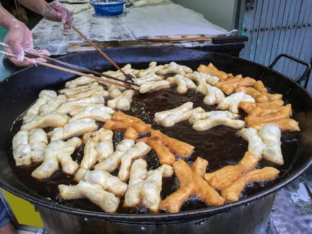 Hands holding chopsticks  fried Deep-Fried Dough Stick, Patongko in pan of hot cooking oilの写真素材