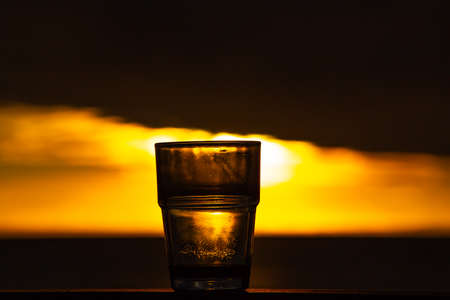 Silhouette glass of coffee with spoon on wood texture at sunrise background, Close up shotの写真素材