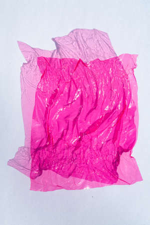 Thin sheet of pink colour cellophane with shiny crumpled surface texture  on white background, Abstract, Light & Shadow conceptの写真素材