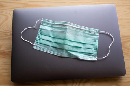 Face mask, Medical mask, Surgical mask on laptop,  Wooden texture background, Close up shot,...