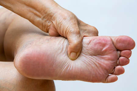 Senior woman suffering from left foot pain, Massaging by her hand in white background, Close up & Macro shot, Asian body skin part, Healthcare, About Massage conceptの写真素材