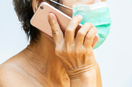Senior woman wearing face mask, Medical mask, Surgical mask, Hand holding smartphone in white...