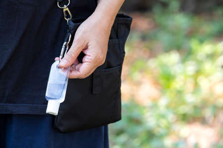 Woman's hands using portable wash hand sanitizer gel pump dispenser with alcohol gel sanitizer in bokeh green, Shoulder bag, Close up shot, Select focus, Prevention from covid19, Bacteria, Healthcareの写真素材