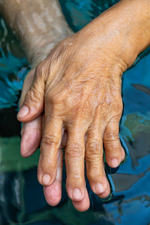 Senior woman's hands washing her hands in step 1 in bokeh blue pool  background, Close up & Macro shot, Selective focus, Prevention from covid19, Bacteria, healthcare concept, 7 step wash handの写真素材