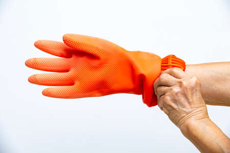 Senior woman's hands wearing orange rubber protective glove in white background, Close up shot, Prevention from covid19, Coronavirus, Bacteria, Healthcareの写真素材