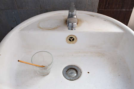 Dirty white washbasin, Clogged drain, Glass, Wooden spoon, Bathroom Cleaning conceptの写真素材