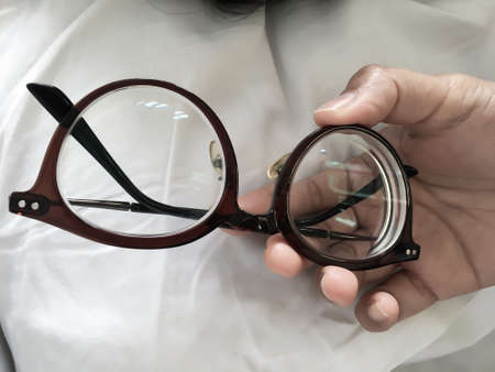 Woman's hand holding   shortsighted or nearsighted eyeglasses on white pillow, white bed background, Close up & Macro shot, Selective focus, Optical conceptの写真素材