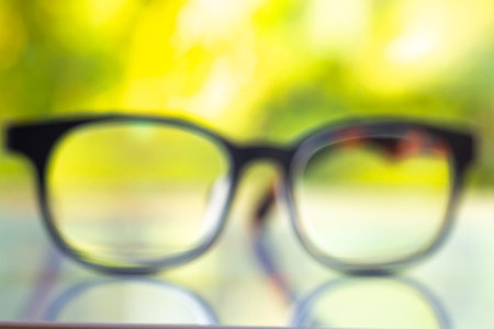 Blurred black shortsighted or nearsighted eyeglasses on white acrylic table, Bokeh green garden background, Close up & Macro shot, Selective focus, Reflection, Optical conceptの写真素材