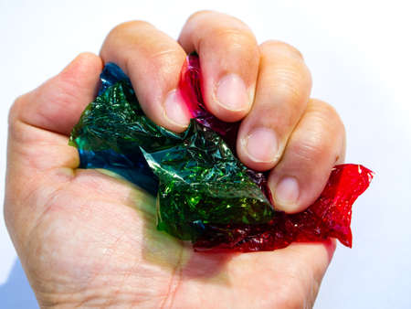 Woman' hand grasping thin sheet of multi coloured cellophane with shiny crumpled surface texture on white background, Abstract, Light & Shadow conceptの写真素材