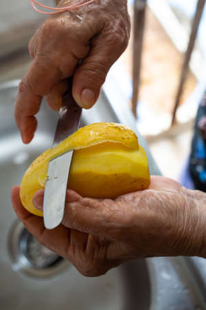Senior woman's right hand using knife peeling sweet yellow mango in sink background, Close up shot, Selective focus, Thai traditional fruitの写真素材