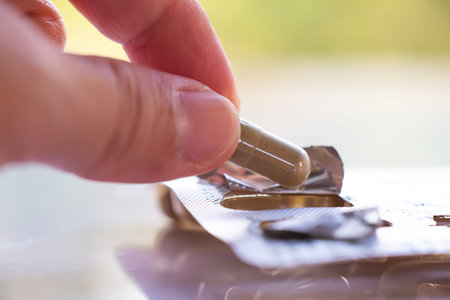 Woman's left hand pick up Andrographis paniculata herbal antipyretic capsules on white acrylic, Bokeh green garden background, Close up & Macro shot, Selective focus, Healthcare conceptの写真素材