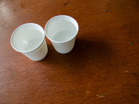 Two paper cups of water on wooden table background, Close up and macro shotの写真素材