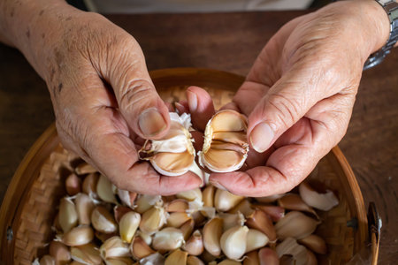 Senior man's hands peeling Garlic or Allium sativum on wood background, Kitchen Process concept