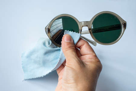 Woman's right hand cleaning brown eyeglasses by microfibre cleaning cloths, On white background, Close up & Macro shot, Selective focus, Optical conceptの写真素材