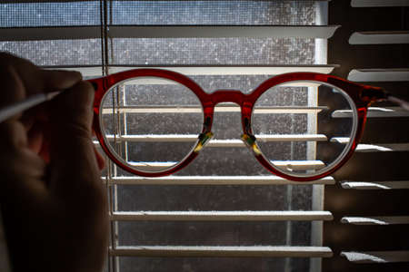 Woman's hand holding   shortsighted or nearsighted eyeglasses with Dust blinds inside a window, Dust and Dirty mosquito wire screen window, Light & Shadow shot, Close up shot, Selective focusの写真素材