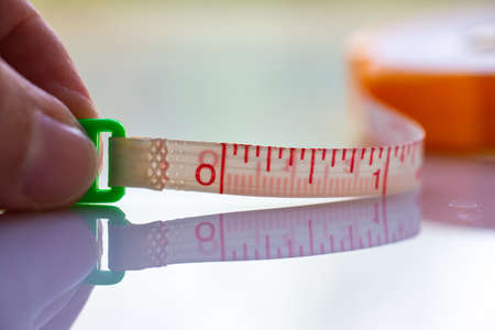Woman's left hand hold Measure Tape ruler metric measurement, Metric ruler, White acrylic background, Close up and macro shot, Selective focus, Creative idea conceptの写真素材
