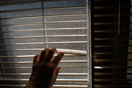 Woman's left hand opening dust blinds inside a window, Blurred dust and Dirty mosquito wire screen...