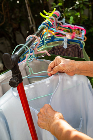Senior woman' hand dry blue clothes in the sun with Colourful plastic clothes hang on stainless...