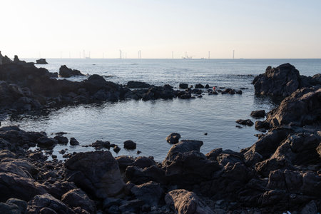 Coastal landscape with wind turbines and rocks in the evening of Jeju Island, South Korea