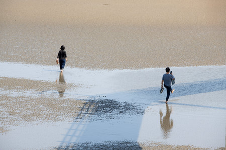 Tourists walking on the beach with reflections in the water.の写真素材