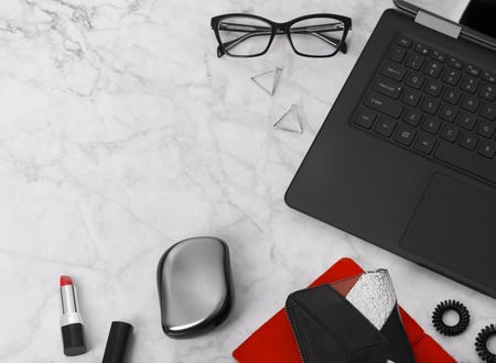 Flat lay workspace with laptop, planner, glasses, mobile phone, ear rings, hair tie, comb and lipstick. Stylish office marble desk. Beauty blogger concept.の写真素材