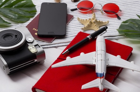 Flat lay travel concept: planner, passport, smartphone, camera, pen, star fish and monstera leaves on white wooden background. Summer vacation objekts.の写真素材