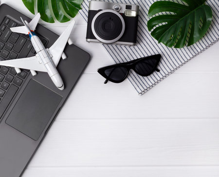 Travel flatlay: laptop, camera, sunglasses, monstera leavs, plane, and towel on wooden table with copy space. Planning summer vacation concept. Summer workcpace.の写真素材