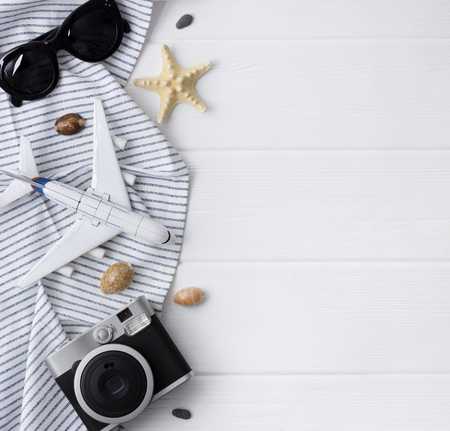 Time to travel concept. Camera, plane, sunglasses, monstera leavs, plane, star fish and towel on white wooden table. Vacation background flat lay with copy space.の写真素材