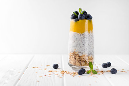 Glass of yogurt with chia seed, blueberries and mango mousse and oatmeal on a white wooden table. Concept of healthy eating, dieting, fitness menuの写真素材