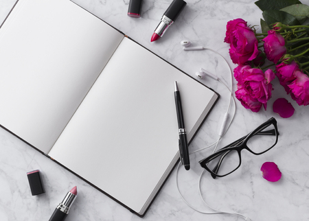 Pink lipstick, headphones, glasses and roses bouquet with blank notepad on white background.の写真素材