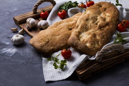 Tasty fresh tandoori bread on wooden tray with tomato, garlic and parsley. National georgian cuisine and food. Copy space for text. Top view or flat lay.の写真素材