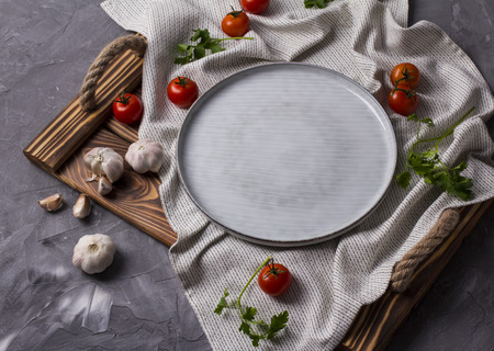 Empty plate on a tray with farmers tomatoes, garlic and parsley at gray background with copy spaceの写真素材