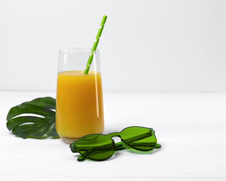 Beach concept with orange juice, straw, sunglasses, monstera leaf. Summer accessories on white wooden tableの写真素材